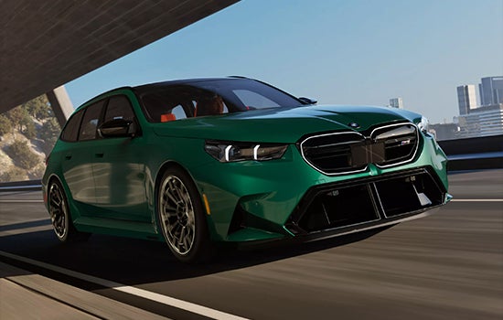 Green BMW M5 Touring driving on a city road. | BMW of Devon in Devon PA